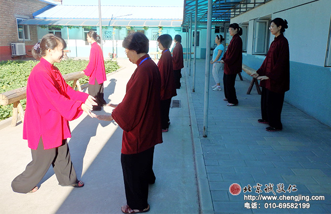 清晨阳光明媚，红衣绿叶蓝天；专业太极拳老师认真指导学员太极定式练习。